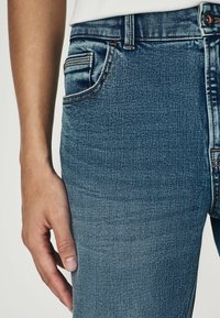 Denim jeans in medium blue met subtiele vervaging, voorzien van een voorzak, contrasterende stiksels en een gladde, gestructureerde afwerking.