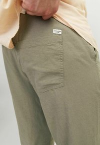 Olive krāsas bikses ar teksturētu audumu, kurām ir aizmugurējā kabata un mazs balts labele ar uzrakstu "JACK&JONES."