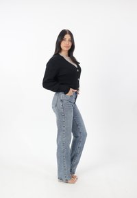 Svart stickad cardigan med långa ärmar och V-ringning, med två knappknäppningar i fram. Kombineras med ljusblå hög midja jeans.