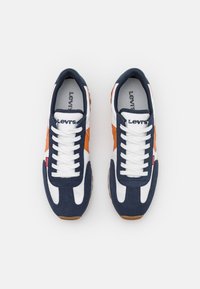 Die Sneakers von Levi's bestehen aus einem navyblauen und weißen Obermaterial mit orangefarbenen Akzenten, runden Schnürsenkeln und einer braunen Gummisohle. Auffälliges Logo auf der Lasche.