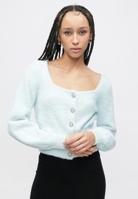 Γαλάζια χνουδωτή ζακέτα με τετράγωνο ντεκολτέ, μακριά μανίκια και τρία διακοσμητικά ασημένια κουμπιά στο μπροστινό μέρος. Διαθέτει εφαρμοστή γραμμή.