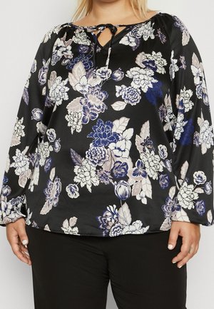 Zwarte blouse met lange mouwen met blauwe, witte en beige bloemenpatronen, voorzien van een keyhole-halslijn met strikdetail, gedragen met zwarte broek.