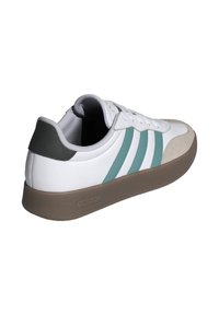 Zapatilla deportiva blanca con franjas en color teal, puntera de ante y suela de goma marrón. Presenta un cuello acolchado y un diseño con cordones en la parte delantera.
