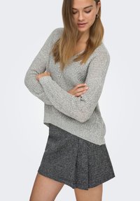 Pull en tricot gris clair avec col en V et manches longues, associé à une jupe plissée gris foncé. Tissu texturé et coupe décontractée.