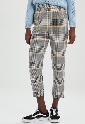 Pantalons à carreaux noir et blanc avec des accents jaunes, coupe courte, design ajusté et texture lisse, associés à des baskets noires.