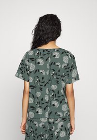 Krátký rukáv, zelený top s květinovým vzorem v bílé a černé barvě. Lehce materiál s volným střihem a kulatým výstřihem.