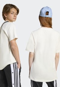 T-shirt en coton blanc à manches courtes, coupe décontractée, vue de face et de dos. Assorti à un pantalon noir avec des rayures blanches sur les côtés.
