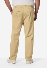 Chinos beige leggeri con una vestibilità rilassata, dotati di tasche posteriori, dettagli di cucitura discreti e risvolti, abbinati a sneaker bianche.