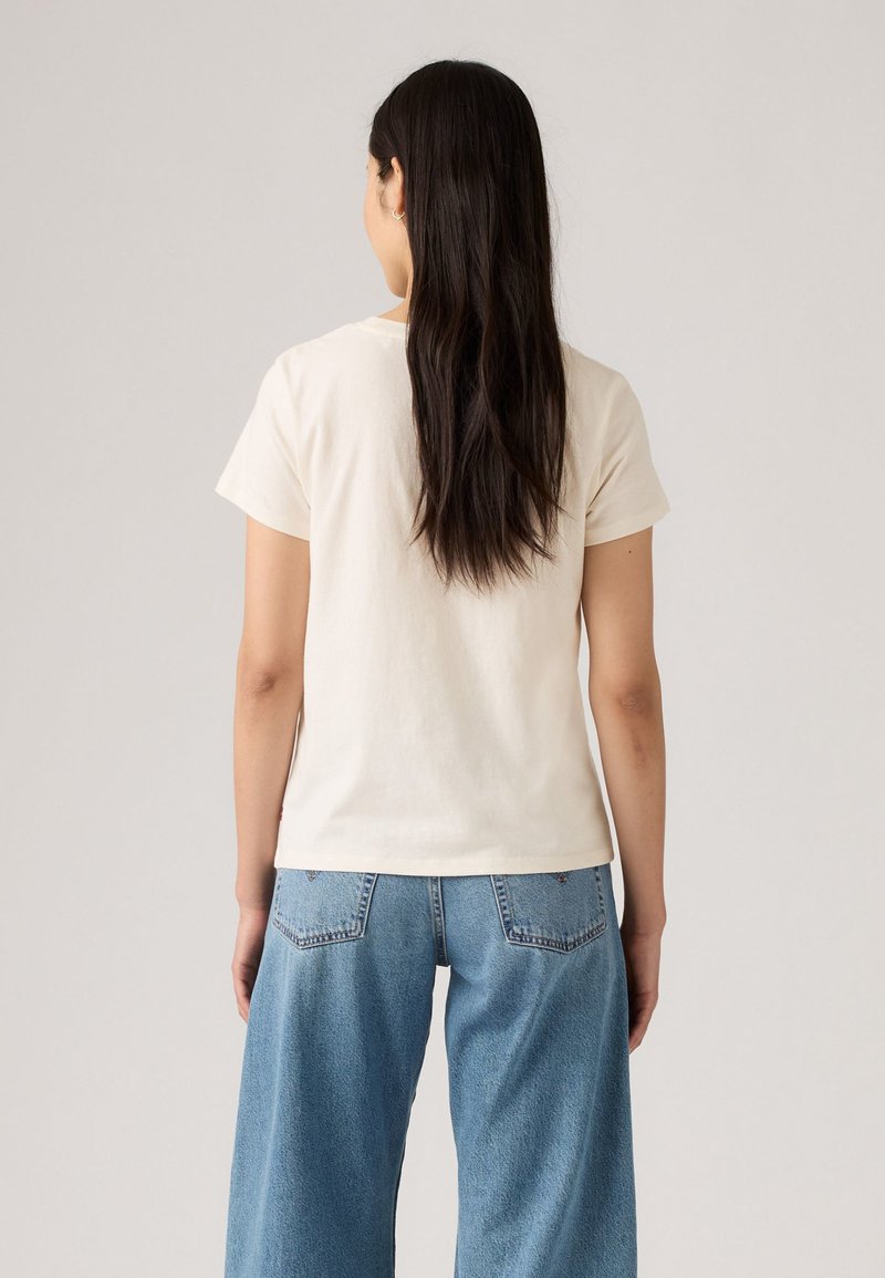 T-Shirt aus Baumwolle mit kurzen Ärmeln in hellem Creme, kombiniert mit lässigen blauen Jeans im Loose-Fit-Stil mit Seitentaschen und hoher Taille.