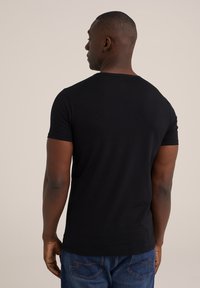 Camiseta negra de manga corta con cuello redondo, hecha de una suave mezcla de algodón, combinada con jeans de mezclilla azules que tienen bolsillos traseros curvados.