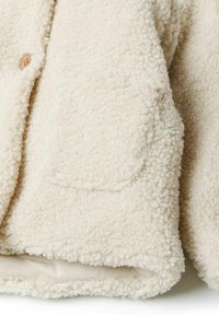 Giacca in pile color crema con superficie morbida e texturizzata, chiusura a bottoni e tasche laterali. Orlo arrotondato confodera liscia.