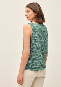 Top verde senza maniche con un motivo a onde, realizzato in tessuto morbido, con scollatura rotonda e vestibilità rilassata, abbinato a pantaloni chiari.