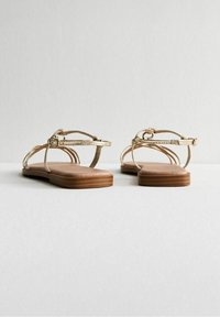 Gouden strapsandalen met een platte bruine zool, voorzien van een minimalistisch ontwerp, een verstelbare enkelband en gestructureerde metallic banden.
