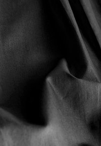Tissu noir drapé avec une texture douce et lisse ; quelques plis créent des ombres, mettant en valeur la profondeur et la dimensionnalité de la surface du matériau.