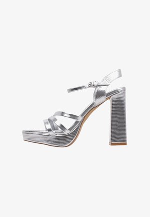 Sandalias de tacón alto plateadas con un acabado texturizado, que presentan múltiples tiras, un cierre de hebilla y un tacón cuadrado grueso.