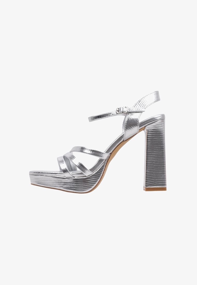 Sandales à talons hauts en argent avec une finition texturée, présentant plusieurs lanières, une fermeture à boucle et un talon large.