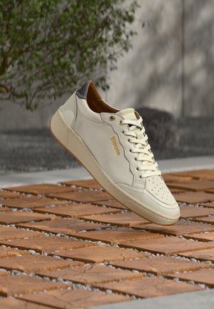 Baskets en cuir blanc avec logo doré, bout perforé et semelle extérieure beige. Présentent un accent bleu marine au talon et des lacets plats blancs.
