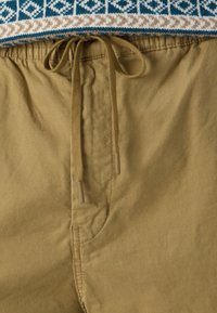 Pantaloni scurți din bumbac khaki cu talie cu șnur, având o textură netedă și buzunare laterale. Top tricotat decorativ cu model în nuanțe de albastru și bej.
