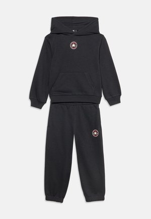 Μαύρο φούτερ με κουκούλα και matching φόρμα με μικρά στρογγυλά λογότυπα αστεριών στο στήθος και στο μηρό, εμφανίζεται σε λευκό φόντο.