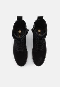 Bottines en daim noir avec fermeture à lacets, fermeture éclair sur le côté et coutures contrastées. L'intérieur présente un logo doré sur une semelle intérieure noire.