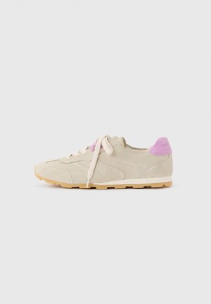 Beige suede sneaker with white laces, light brown sole, and a pink heel tab with subtle stitching details, shown from the outer side.