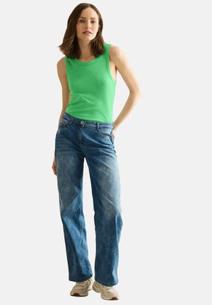 Groene mouwloze top, lichtblauwe versleten jeans en beige sneakers. Casual pasvorm met een eenvoudig ontwerp en schone lijnen.