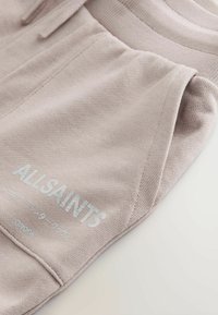Hellrosa Jogginghose aus weichem Baumwollmischgewebe. Mit seitlicher Tasche und hellblau gedrucktem "ALLSAINTS"-Logo.