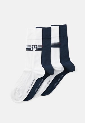 Set van drie paar sokken; twee witte met ribbelstructuur en logo, één marineblauwe. Allemaal hebben ze contrasterende boorden en branding op de zolen.