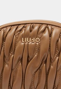 Sac en cuir marron avec une texture matelassée. Le logo doré "LIU JO" est mis en avant, agrémenté de détails de couture assortis.