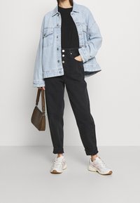 Světle modrá denimová oversized bunda, černé tričko, černé kalhoty s vysokým pasem, bílé sportovn í boty a hnědá kabelka s vzorem.