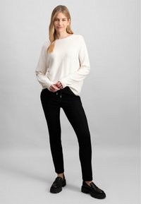 Tejanyagú, hosszú ujjú krém színű pulóver, fekete karcsú nadrággal párosítva. A lábbeli fekete platform mokaszin, amely egy elegáns, laza megjelenést kölcsönöz.