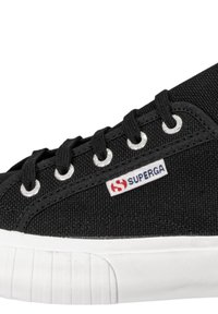 Sneaker nera in tela con suola in gomma bianca, dotata di occhielli metallici, lacci neri e un'etichetta logo visibile sul lato.