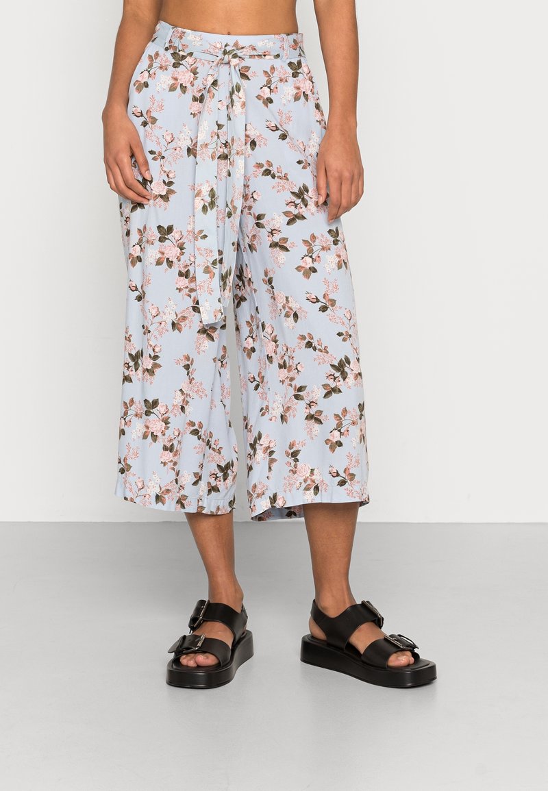 Floral print culotte pants in light blue fabric, featuring a tie waist and wide legs. Worn with black platform sandals with buckles.