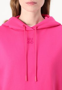 Felpa rosa brillante con cappuccio, dotata di un cordino, logo "HUGO" ricamato, texture morbida e vestibilità rilassata. Tessuto leggero adatto per un abbigliamento casual.