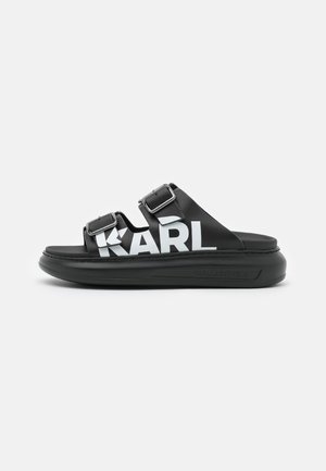 Zwarte slippers met dubbele verstelbare banden, voorzien van een vet wit "KARL" logo en een gestructureerde zool voor grip en comfort.