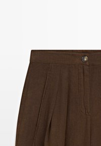 Pantaloni marroni a vita alta con pieghe frontali, tasche laterali e chiusura con bottone in vita.