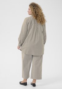 Ensemble en tissu rayé beige comprenant une chemise ample avec un pli au dos et un pantalon court assorti. Porté avec des ballerines noires.