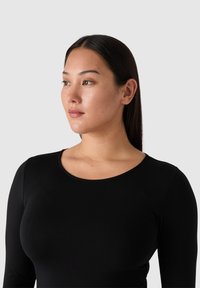 Mustapaita pitkällä hihalla, jossa on avara kaula-aukko. Sileä kankaan rakenne ja tiukka muotoilu, joka korostaa kehon muotoa ilman koristeluja.