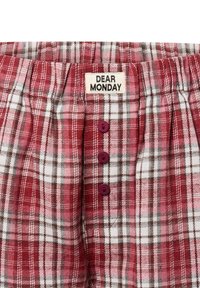 Rot-weißer Karostoff mit grauen Akzenten, elastischem Bund, drei burgunderfarbenen Knöpfen und einem Etikett "DEAR MONDAY" an der Oberseite.