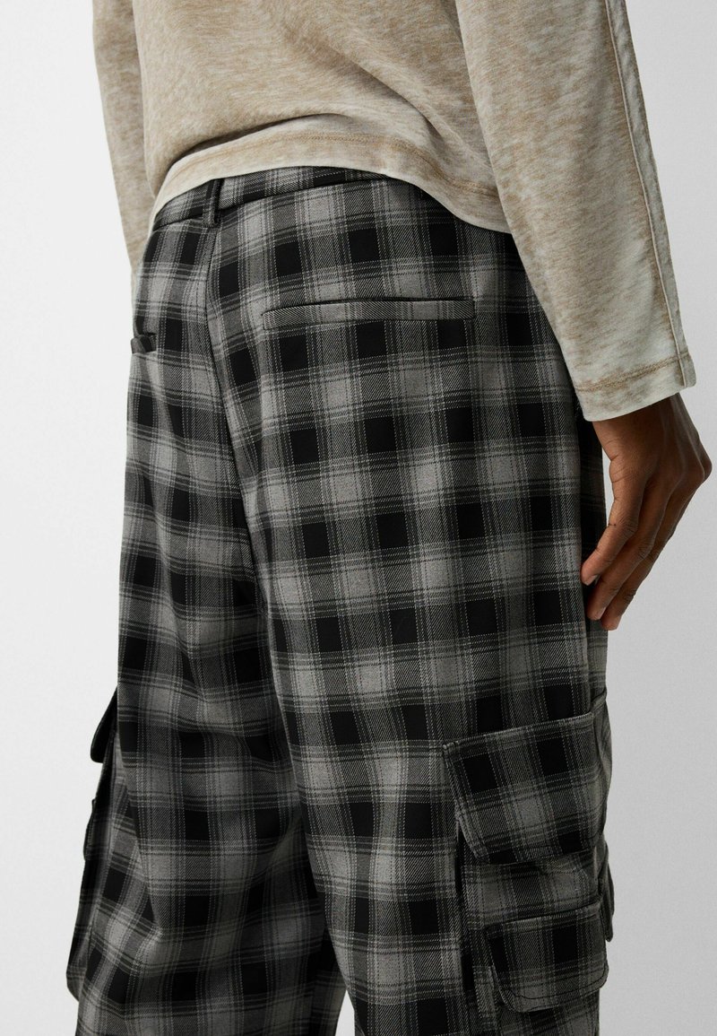 Pantalones cargo de cuadros en negro y gris con bolsillos laterales, que presentan una tela texturizada y un corte ajustado, mostrados desde un ángulo trasero.