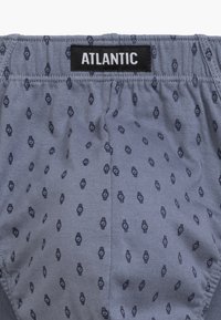 Szare bokserki z powtarzającym się wzorem zegarów w ciemnoniebieskim kolorze. Tkanina wydaje się miękka, z elastycznym paskiem z oznaczeniem "ATLANTIC."