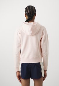 Svijetlo ružičasta hoodie s kapuljačom, rebrastim manžetama i rubom, u kombinaciji s mornarskim kratkim hlačama s svijetlim akcentima. Glatka tekstura, ležeran dizajn.