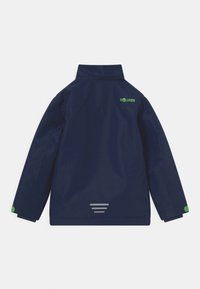 Casaco impermeável azul-marinho com colarinho alto, logótipo verde nas costas, detalhes refletivos e punhos elásticos para um ajuste seguro.