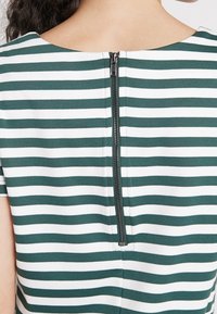 Zeleno-bílý pruhovaný top s kulatým výstřihem a centrálním zadním zipem. Vyrobeno z hladkého materiálu s pohodlným střihem.