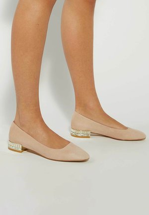 Beige suede ballet flats with a low block heel featuring a clear geometric accent. Rounded toe and streamlined, smooth design.