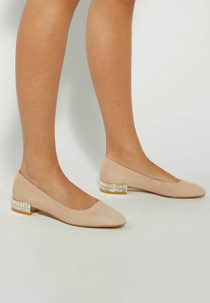 Beige suede ballet flats with a low block heel featuring a clear geometric accent. Rounded toe and streamlined, smooth design.