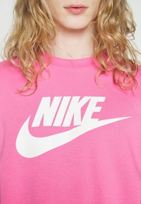 Rosa Nike-hoodie i en bomullsblandning med en stor vit logotyp och swoosh, ribbad halsringning och mjuk textur.