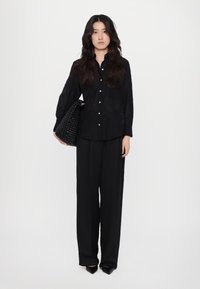 Zwarte, lange mouw, knoopsluiting shirt gecombineerd met losse zwarte broek. Een gestructureerde zwarte geweven tas en spitse zwarte hakken maken de outfit compleet.