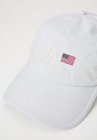 Cappellino da baseball bianco con "USA" e "SAIL GP TEAM" ricamati. Presenta una piccola bandiera americana e un tessuto testurizzato. Visiera arcuata.