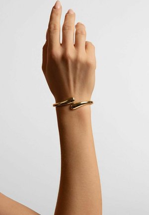 Gold-colored metallic cuff bracelet with a smooth, curved design. Two connected loops create a seamless, minimalist appearance.